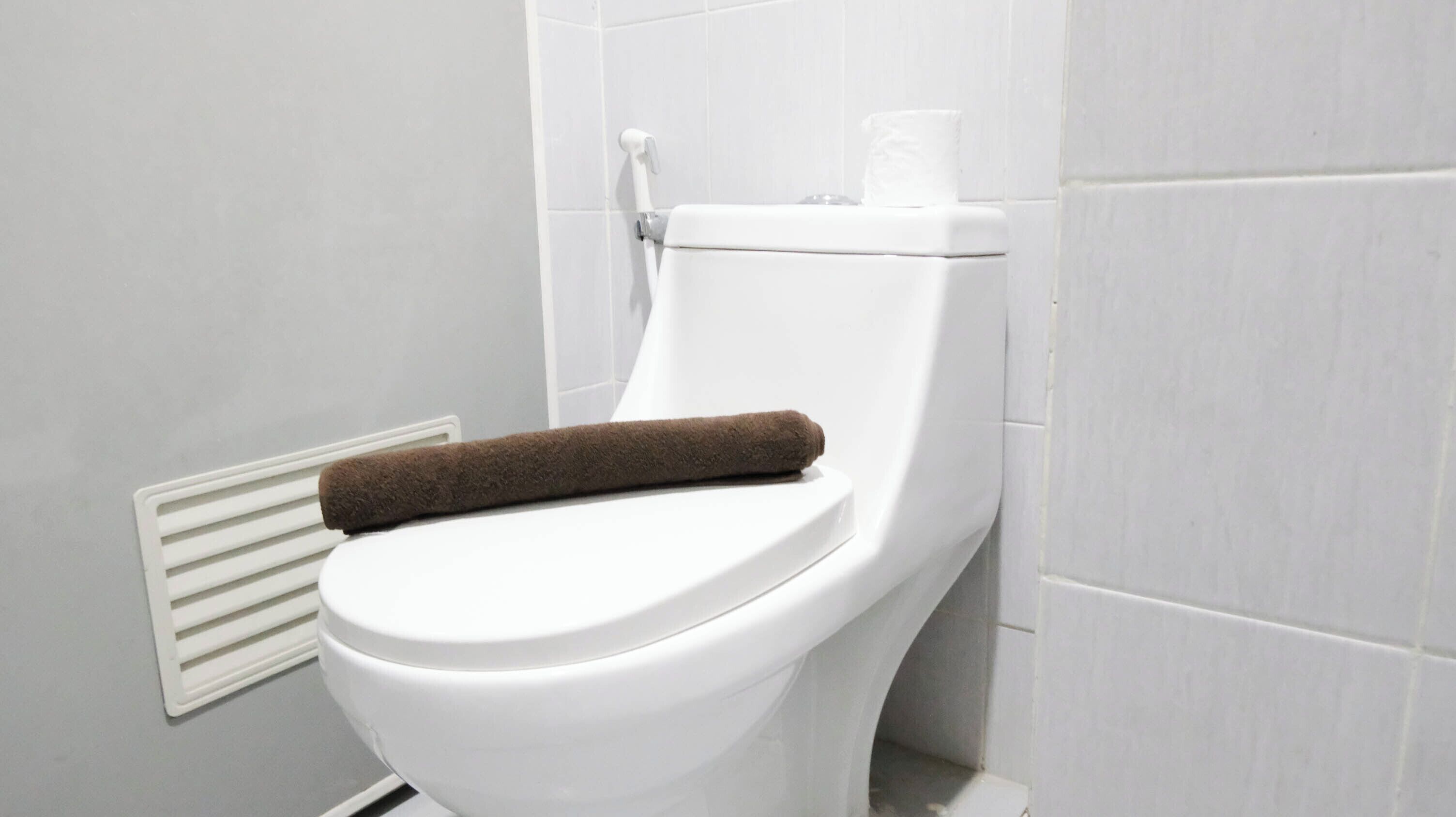 A white toilet with a brown towel on the seat and a toilet paper roll on the tank.
