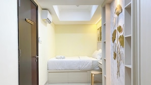 Quarto com cama, um banquinho pequeno, guarda-roupa e luz no teto.