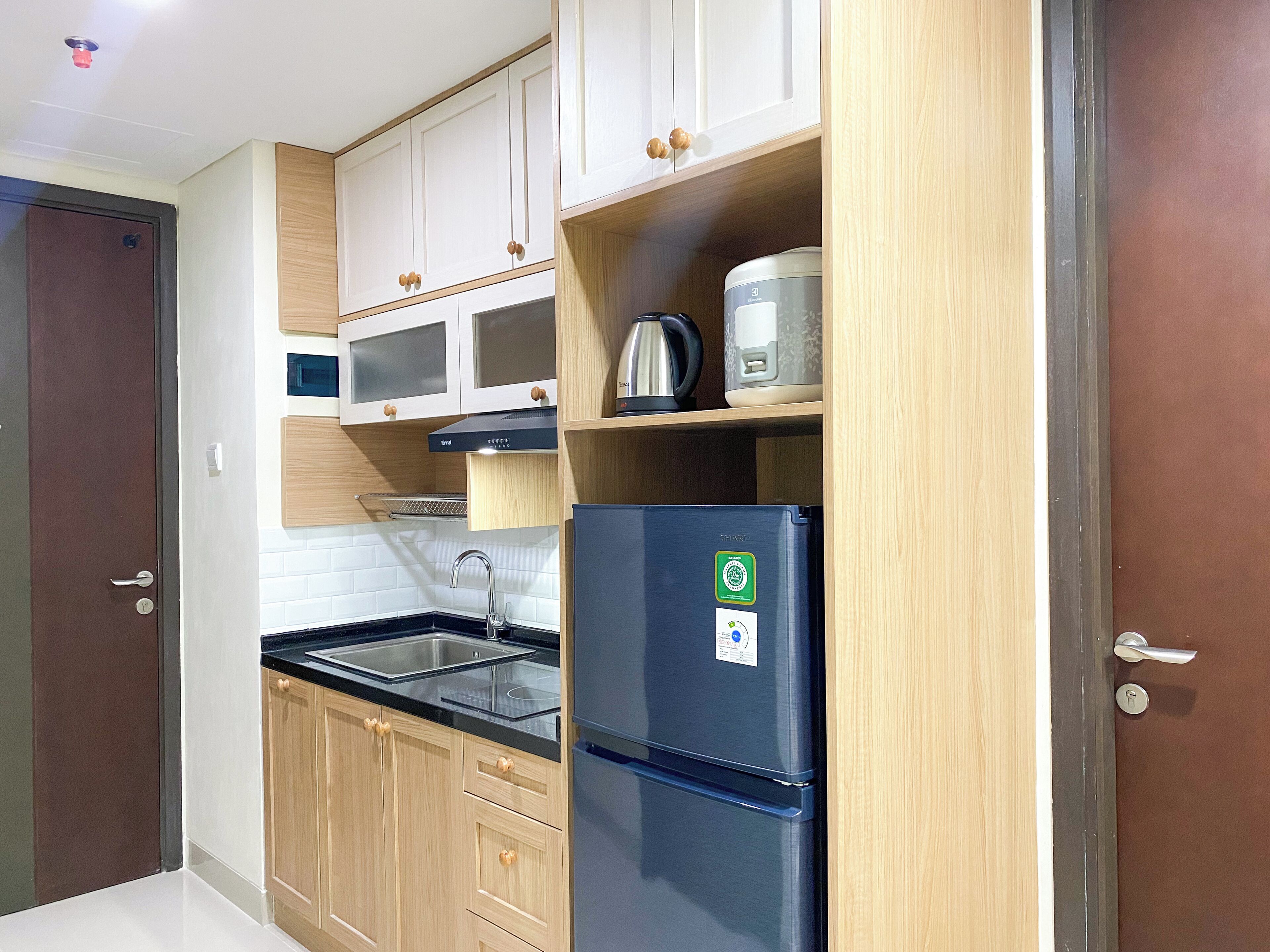 Una cocina compacta con armarios de madera, un lavamanos de acero inoxidable y un microondas integrado.