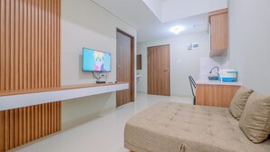 A modern hotel room with a bed, a TV, a kitchenette, and a wooden panel wall. - Modern Look 1BR at LRT City Sentul - Royal Sentul Park Apartment (Bogor)