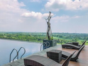 An infinity pool with lounge chairs and a view of a green landscape. - Modern Look 1BR at LRT City Sentul - Royal Sentul Park Apartment (Bogor)