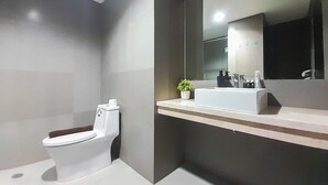 A modern bathroom with a toilet, sink, and mirror. - Comfort Stay 1BR at Patraland Amarta Apartment (Ngaglik)