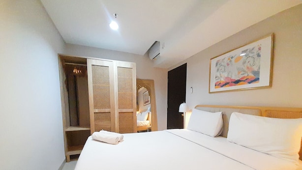 A hotel room with a large bed, a wardrobe, and a painting on the wall. - Comfort Stay 1BR at Patraland Amarta Apartment (Ngaglik)