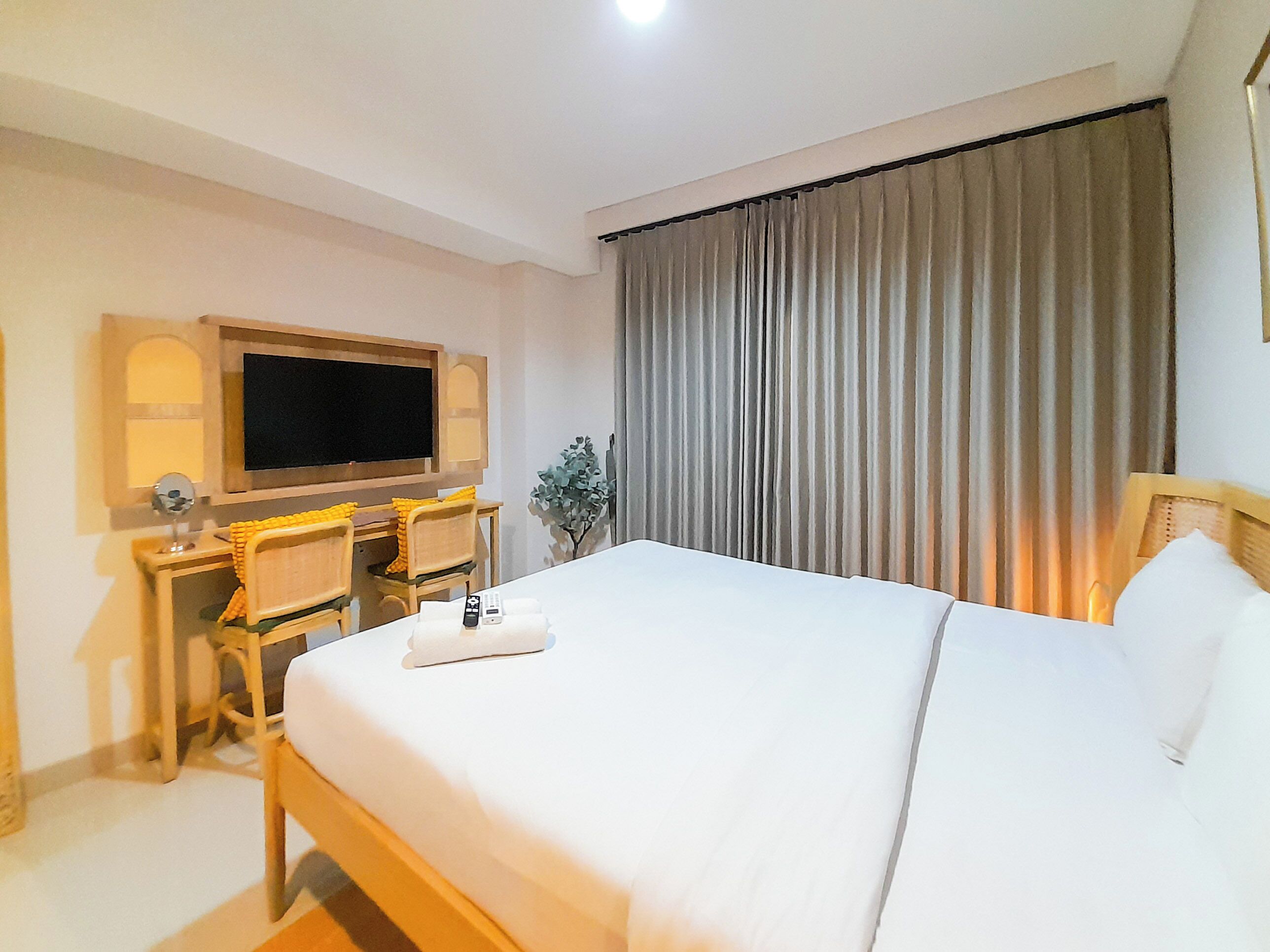 Una habitación de hotel con una cama grande, un escritorio con una silla, un televisor y una ventana con cortinas.