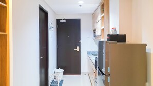 Um corredor estreito com uma porta escura no fim, um frigorífico à direita e um eletrodoméstico branco pequeno perto da porta.