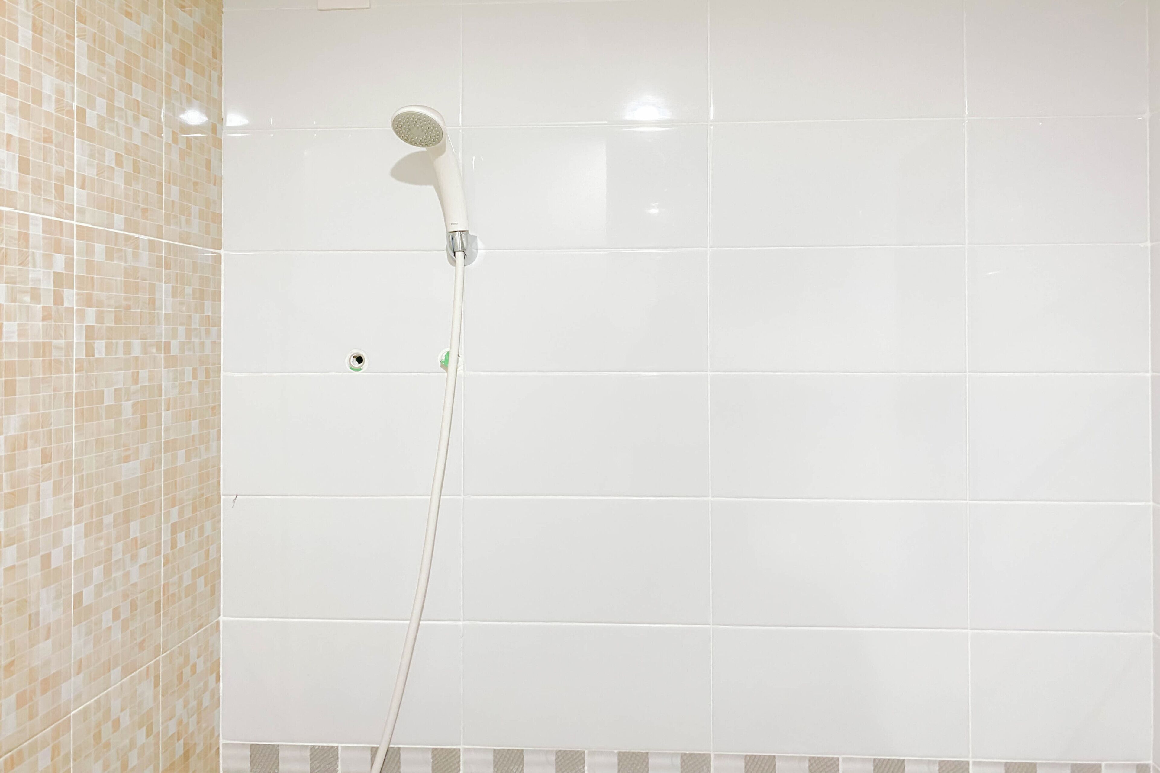 A shower with a handheld showerhead in a bathroom with tiled walls.