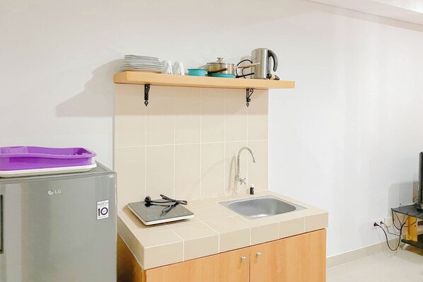 A compact kitchen with a sink, a refrigerator, and a shelf above the countertop. - Homey and Modern 2BR Apartment at Royal Olive Residence (Jakarta)
