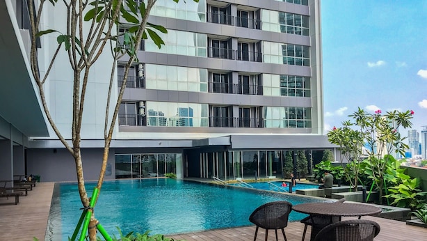 A modern building with a rooftop pool, surrounded by lush greenery and furnished with outdoor seating.