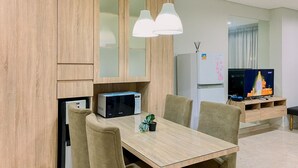 Una sala de estar moderna con un mueble de madera, un microondas, un refrigerador, un televisor y una mesa de comedor con sillas.
