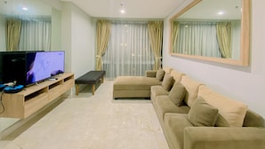 Una sala de estar con un televisor de pantalla plana, un sofá, un banco y un espejo grande en la pared.