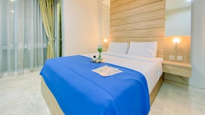Habitación de hotel con cama, mesita de noche, ventana con cortinas y cabecero de madera.