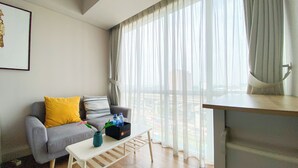 Een moderne woonkamer met een grijze bank, een witte salontafel en uitzicht op een stadsbeeld door dunne gordijnen.