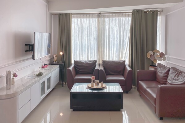Una sala de estar moderna con un televisor de pantalla plana, dos sofás de cuero, una mesa de centro de vidrio y un mueble blanco con objetos decorativos.