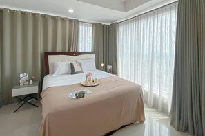 A hotel room with a large bed, a bedside table with a lamp, and a view of the outdoors through sheer curtains. - Spacious and Comfy 2BR Combined at Grand Kamala Lagoon Apartment (Bekasi)