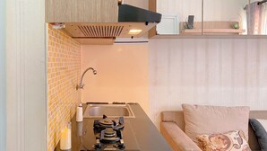 A compact kitchen with a gas stove, a sink, and a tiled backsplash. - Good and Warm 2BR at Green Pramuka City Apartment (Jakarta)