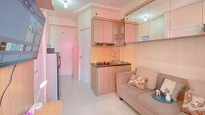 A modern kitchen with wooden cabinets, a built-in oven, and a microwave. There is a dining area with a sofa and a small table. - Good and Warm 2BR at Green Pramuka City Apartment (Jakarta)