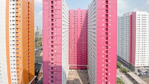 A high-rise building with multiple floors, featuring a central core and a symmetrical facade. - Good and Warm 2BR at Green Pramuka City Apartment (Jakarta)