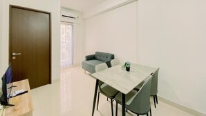 A small, bright room with a dining table, chairs, a sofa, and a door. - Brand New and Homey 2BR at Transpark Cibubur Apartment (Depok)