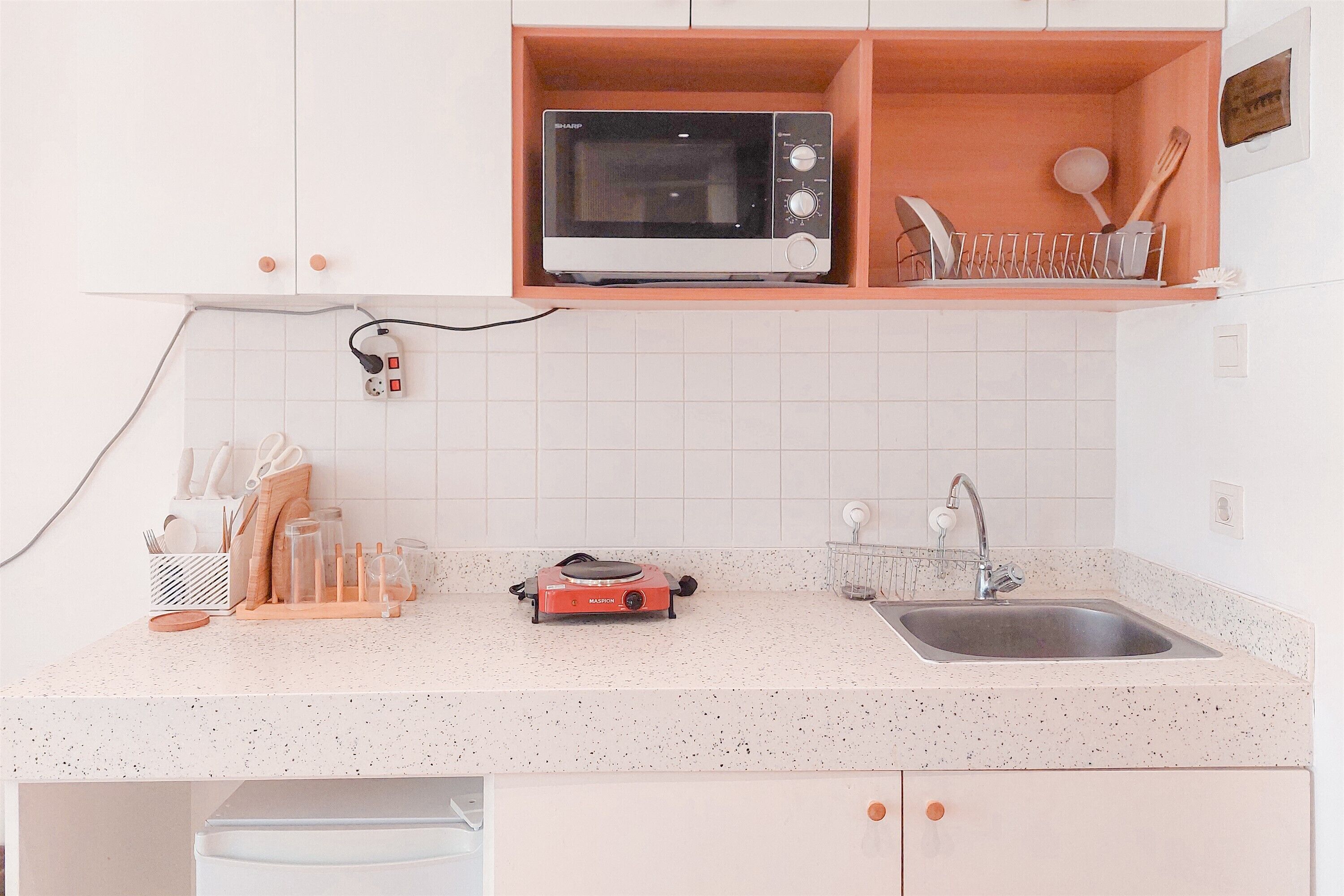 A kitchen with white cabinets, a microwave, a toaster, a sink, and a dish rack.