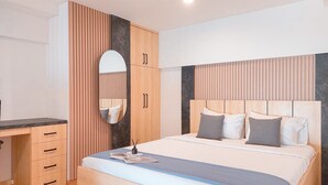 A modern bedroom with a wooden wardrobe, a bed with grey bedding, and a bedside table with a lamp. - Spacious and Comfort Studio Loft at Kingland Avenue Apartment (South Tangerang)