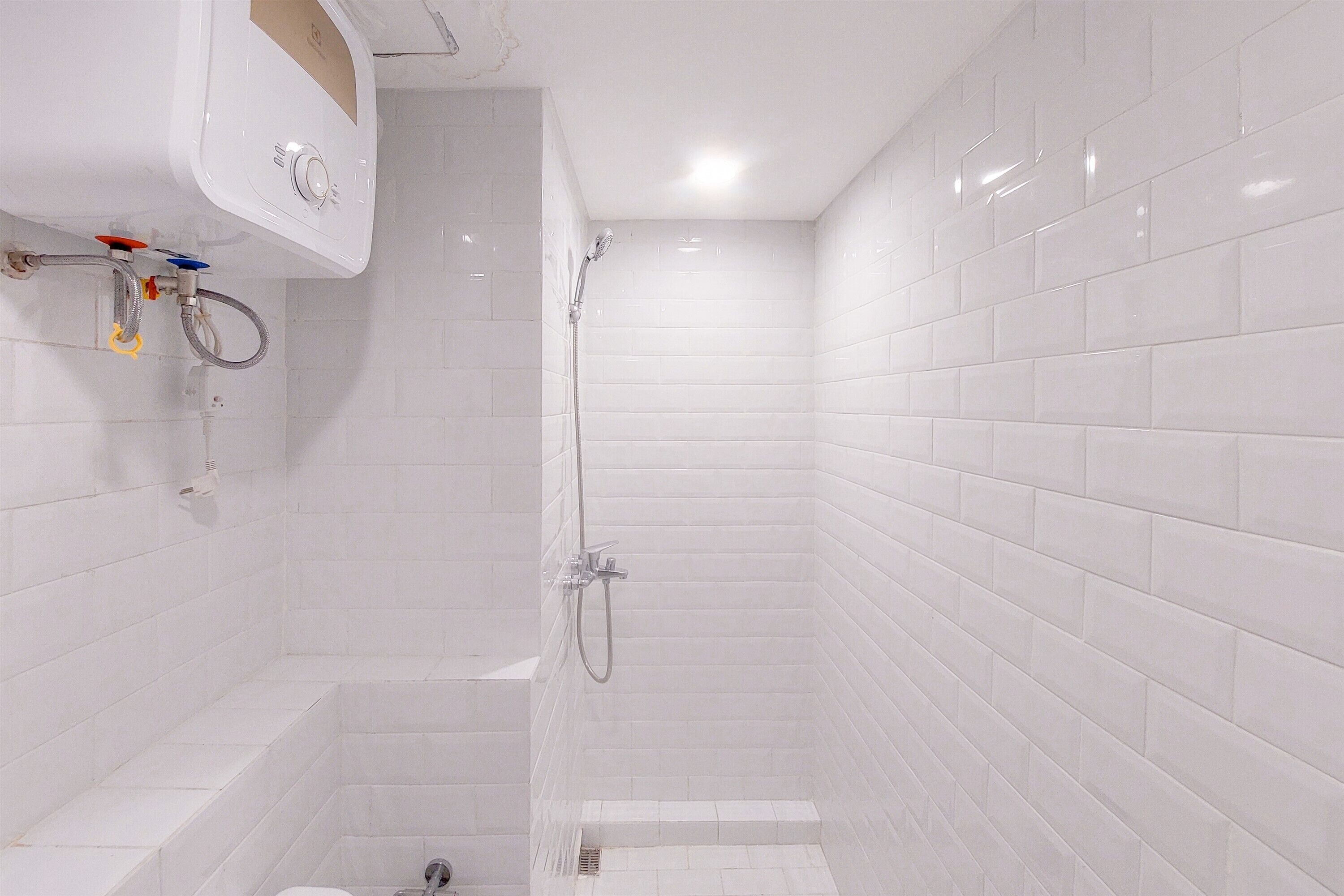 A small, white-tiled bathroom with a shower, a toilet, and a sink.