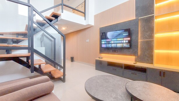A modern living area with a staircase, a flat-screen TV mounted on a wall, and two round tables. - Spacious and Comfort Studio Loft at Kingland Avenue Apartment (South Tangerang)