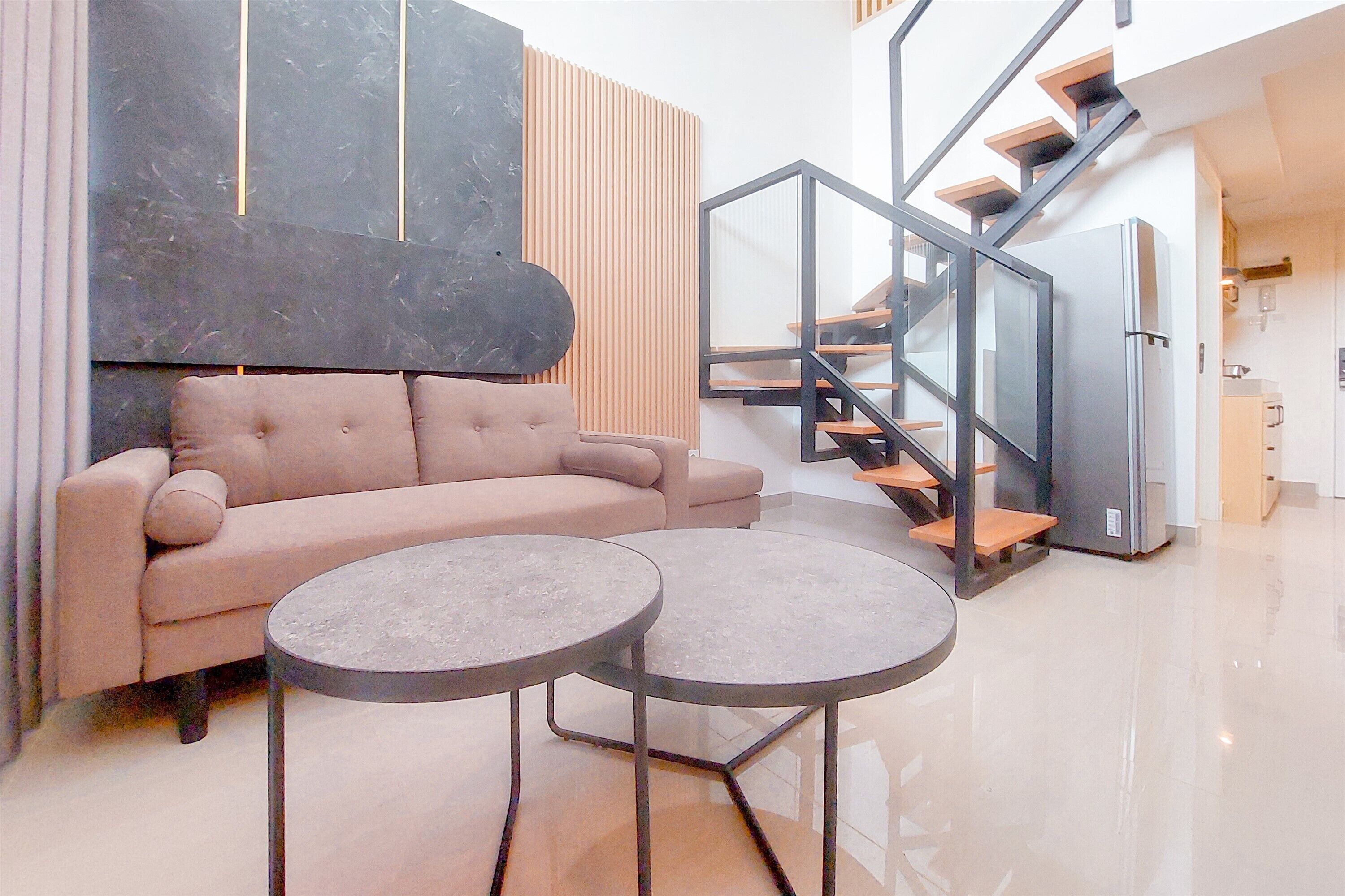 A modern living room with a sofa, two round tables, a black accent wall, and a staircase leading to the kitchen.