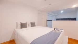 A bedroom with a bed, pillows, a bedside table, and a mirror. - Homey and Comfy Studio Loft at Kingland Avenue Apartment (South Tangerang)