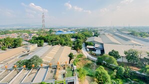 A large industrial area with multiple buildings, including a prominent blue-roofed structure, surrounded by greenery and power lines.