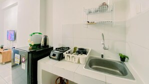 A modern kitchen with white tiles, a stainless steel sink, a kettle, a toaster, and a small refrigerator.