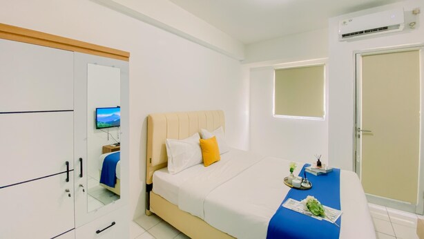 A hotel room with a bed, a wardrobe, a mirror, a television, an air conditioning unit, and a window.