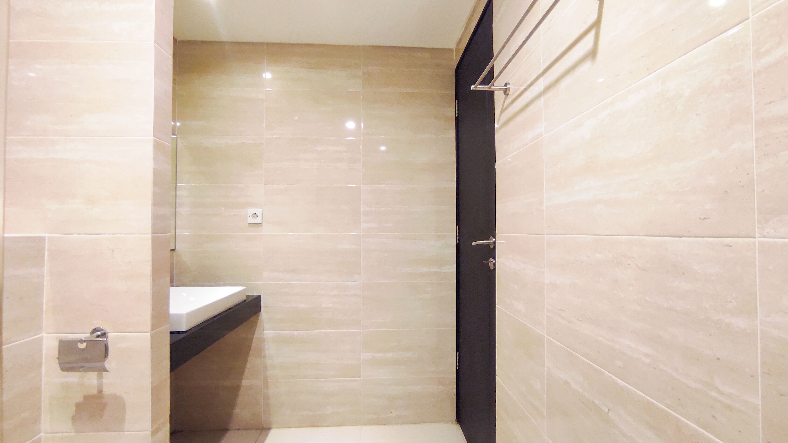 Un baño moderno con azulejos color beige, una puerta negra y un lavamanos blanco.