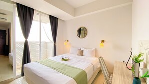 A hotel room with a bed, a round mirror, two wall-mounted lamps, a small table, and a potted plant. - Enjoy Living Studio at West Vista Apartment (Jakarta)