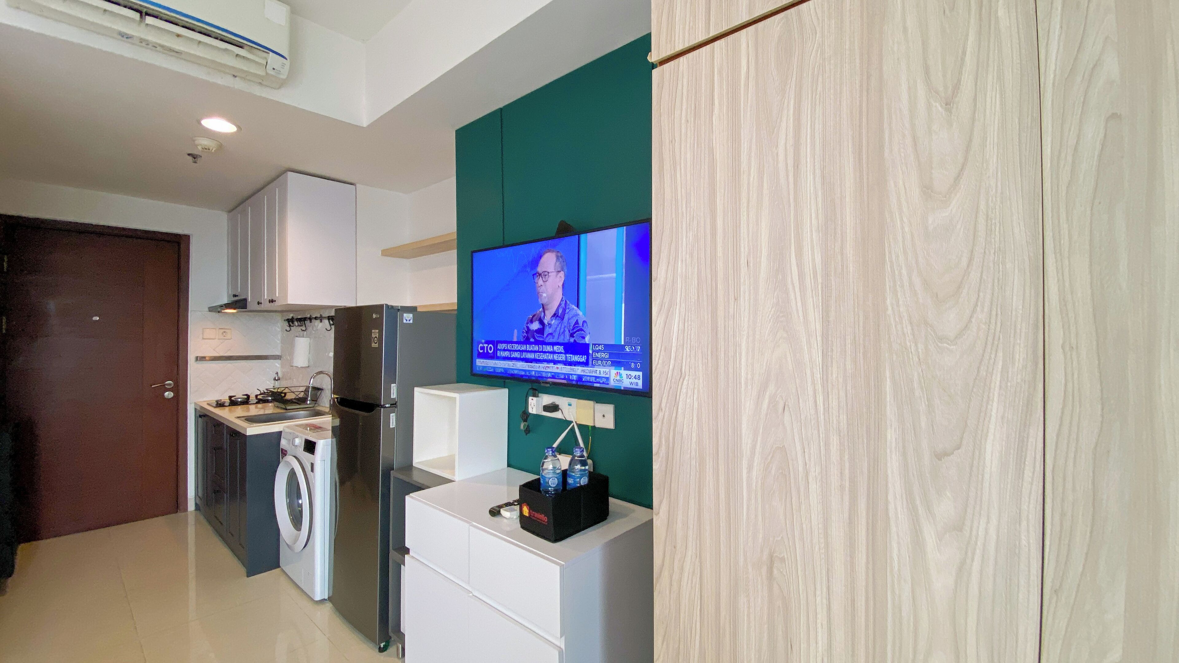 A compact kitchen with a TV, washing machine, and a small fridge.