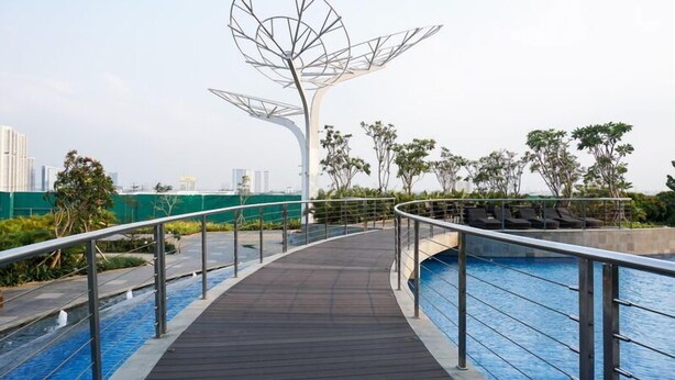 A rooftop pool area with a modern metal sculpture, lounge chairs, and a view of the city skyline. - Enjoy Living Studio at West Vista Apartment (Jakarta)