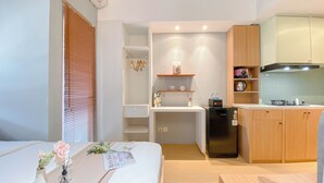 A compact hotel room with a bed, bedside table, a small kitchenette, and a bathroom with a shower.