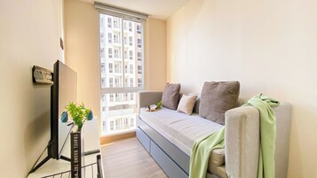 Una sala de estar moderna con un sofá, un televisor de pantalla plana y una ventana con vistas a un edificio.