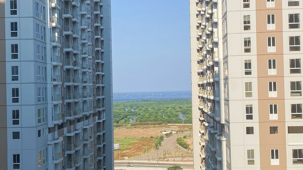 A high-rise residential building with multiple balconies and a clear view of a green landscape and distant cityscape.