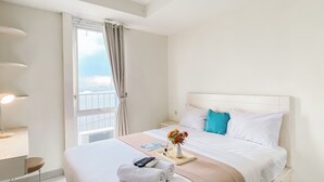A hotel room with a bed, a bedside table, a window with curtains, and a view of the city. - Modern Look and Restful Studio at Azalea Suites Apartment (Cikarang)