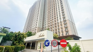A tall hotel with a modern design, featuring a prominent entrance and multiple balconies. - Modern Look and Restful Studio at Azalea Suites Apartment (Cikarang)