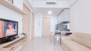 A modern living room with a flat-screen TV, a beige sofa, and a dining area with a table and chairs. - Good Choice and Restful 1BR at Tree Park City BSD Apartment (South Tangerang)