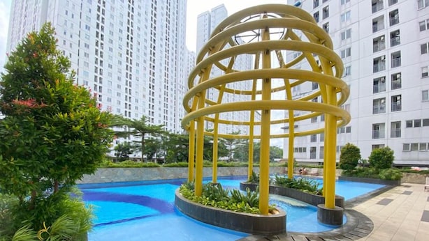 A modern outdoor pool area with a yellow circular structure, surrounded by greenery and high-rise buildings in the background. - Comfy and Minimalist Studio at Bassura City Apartment (Jakarta)
