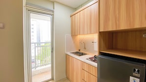 A small kitchen with wooden cabinets, a stainless steel sink, and a black refrigerator. - Comfy and Minimalist Studio at Bassura City Apartment (Jakarta)