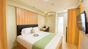 A hotel room with a bed, a desk, a chair, a TV, and an air conditioning unit. - Comfy and Minimalist Studio at Bassura City Apartment (Jakarta)