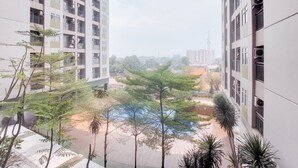 Un edificio residencial alto con varios balcones, un patio con árboles y una vista distante de otros edificios.