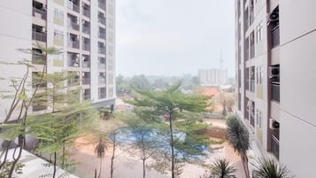 A high-rise residential building with multiple balconies, a courtyard with trees, and a distant view of other buildings.
