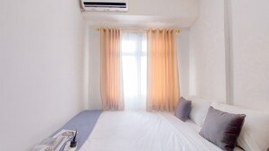 Habitación de hotel con cama, mesita de noche, ventana con cortinas ligeras y equipo de aire acondicionado.
