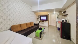 A modern living room with a sofa, a coffee table, and a TV mounted on the wall. - Cozy and Good Place Studio at Taman Melati Sinduadi Apartment (Pogung Lor)
