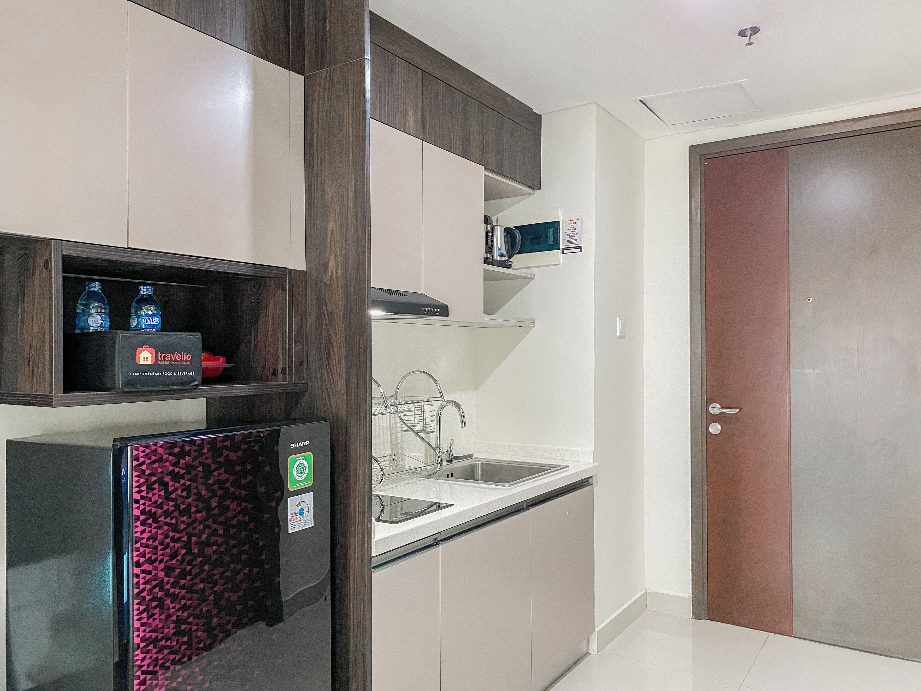 Eine kleine Küche mit Kühlschrank, Mikrowelle und Spüle. Auf der Arbeitsfläche stehen Wasserflaschen und eine kleine Kaffeemaschine.