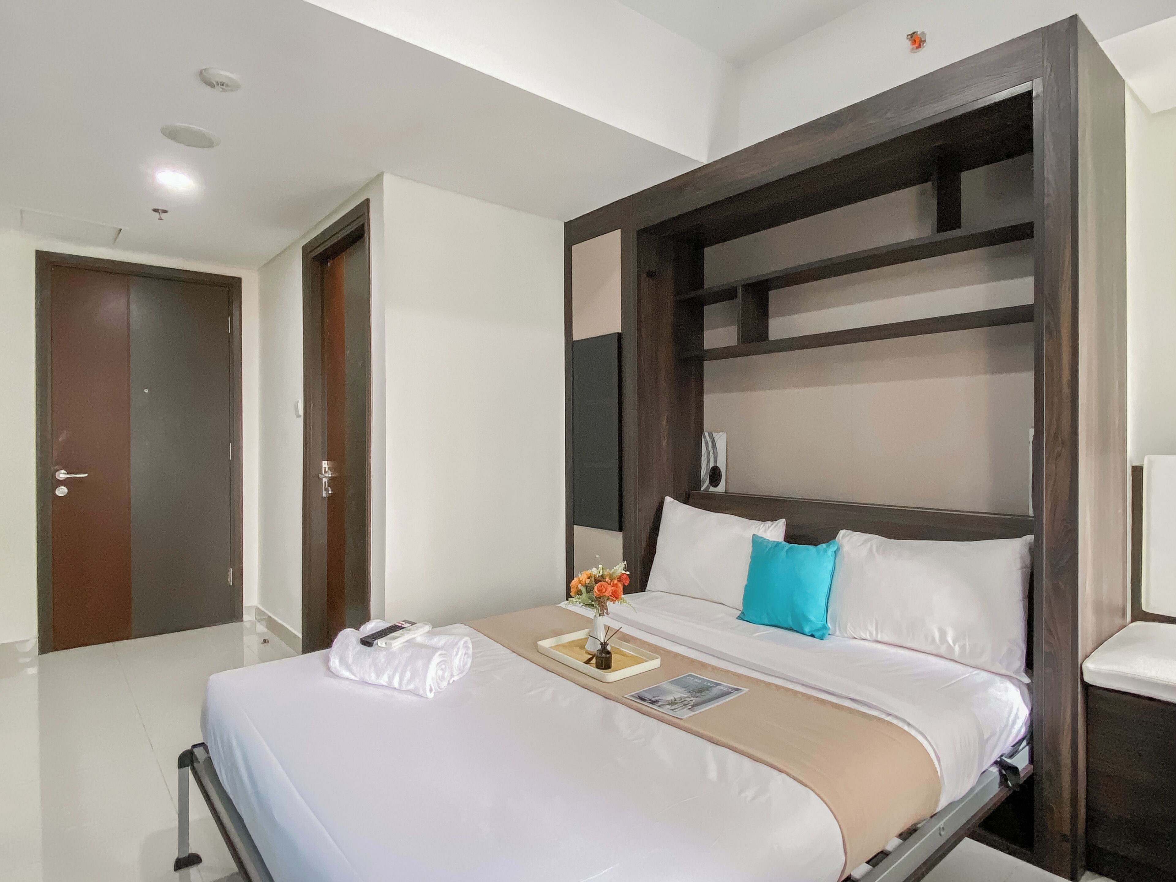 A hotel room with a bed, a bedside table, a lamp, and a door.